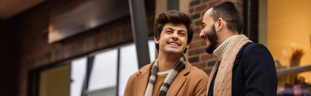 Sakallı eşcinsel adam Bulanık sokakta neşeli ve şık erkek arkadaşına bakıyor. - Fotoğraf, Görsel