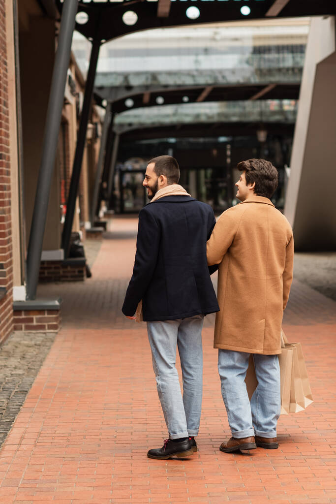 Şehir sokaklarında alışveriş torbaları taşıyan modaya uygun eşcinsel çiftin arka planı. - Fotoğraf, Görsel