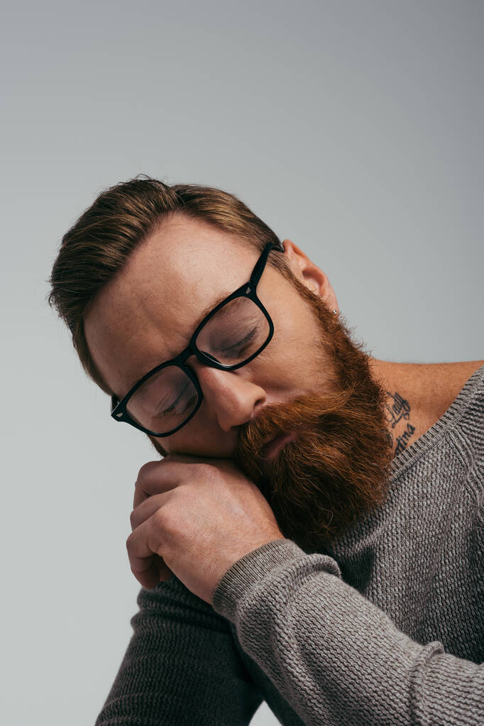 Hombre barbudo en anteojos posando con los ojos cerrados aislados en gris  - Foto, imagen