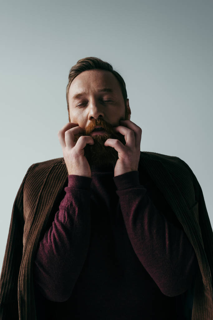 homem de gola alta e blazer arranhando barba isolada em cinza  - Foto, Imagem