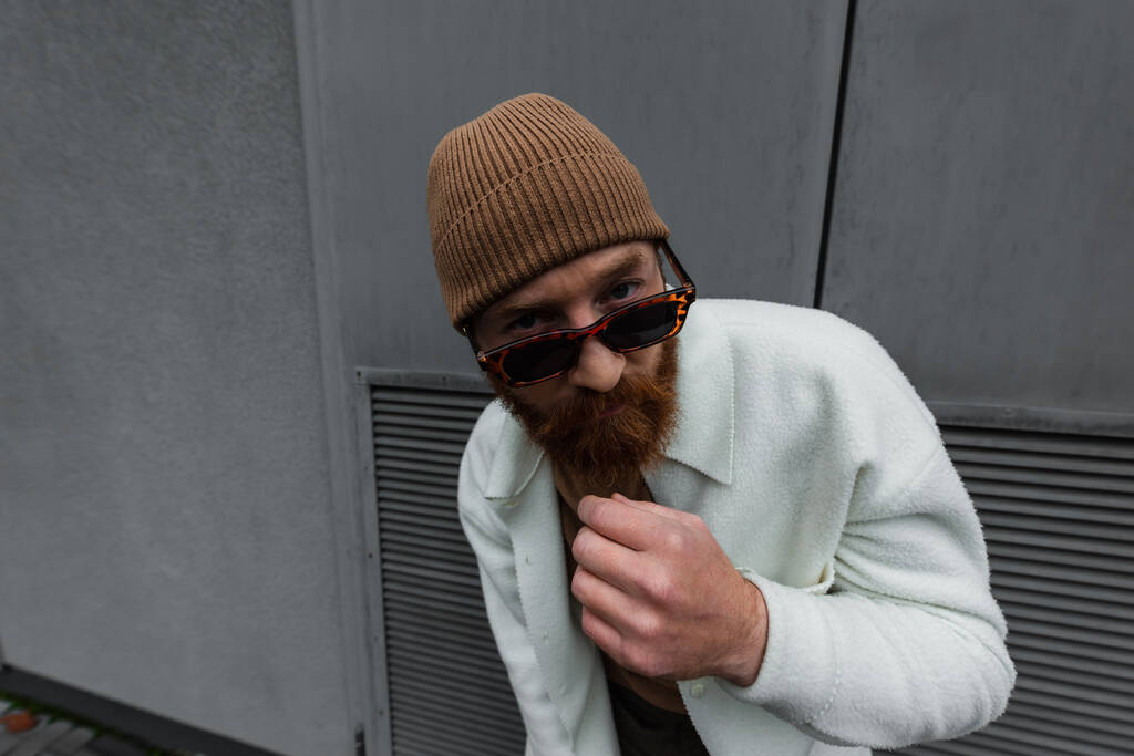 бородатый мужчина в стильных солнцезащитных очках и белой рубашке, смотрящий в камеру  - Фото, изображение