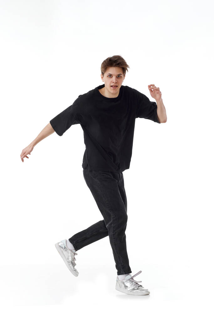 Fröhlicher junger Mann in schwarzem T-Shirt und Jeans, der auf weißem Hintergrund tanzt. Volle Länge - Foto, Bild