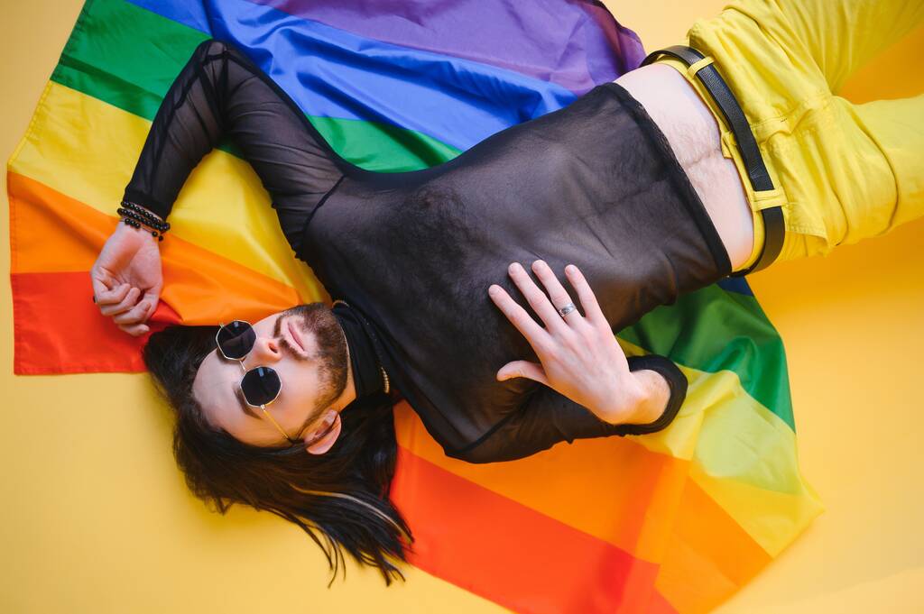 Eşcinsel gurur bayrağı taşıyan eşcinsel adam gülümsüyor ve sarı arka plana bakıyor.. - Fotoğraf, Görsel