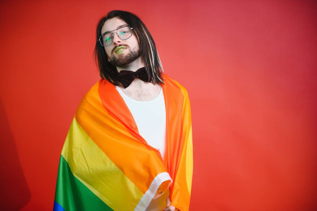 Гей держит радужный полосатый флаг, изолированный на цветном фоне студийного портрета. Люди стиль жизни fashion lgbtq концепция. - Фото, изображение
