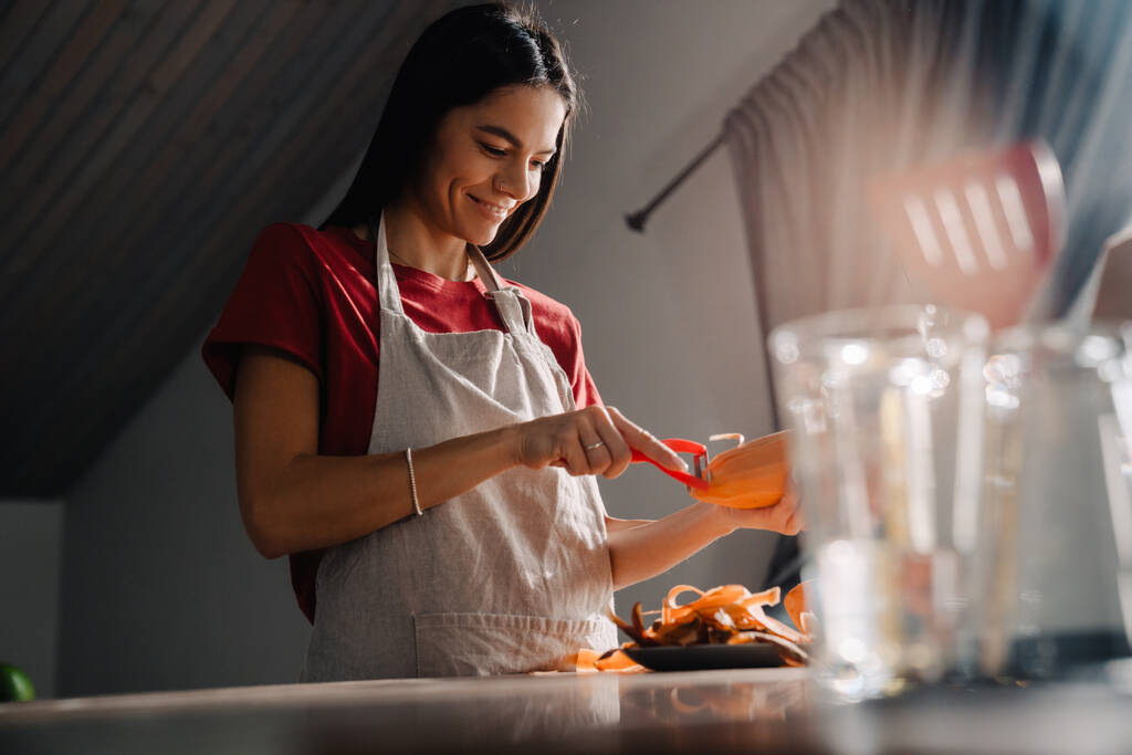 Молодая латиноамериканка чистит сладкий картофель, готовя дома на кухне. - Фото, изображение
