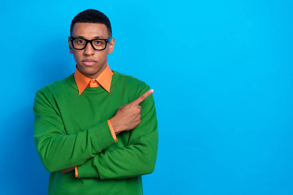 Portrait d'un gars intelligent sérieux et intelligent porter chemise orange sous pull vert indiquant espace vide isolé sur fond de couleur bleue. - Photo, image