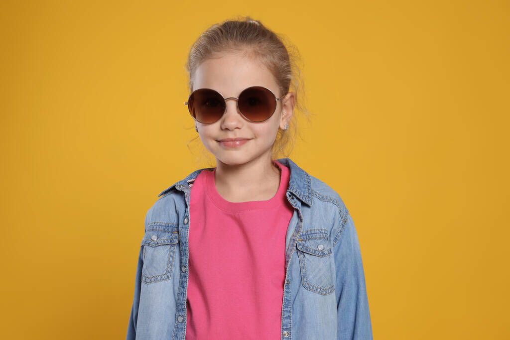 Dziewczyna w stylowych okularach przeciwsłonecznych na pomarańczowym tle - Zdjęcie, obraz