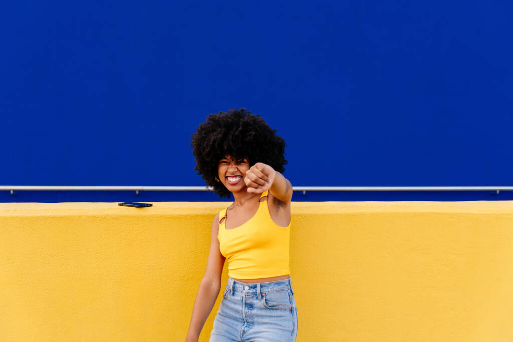 Piękny młody szczęśliwy afrykański kobieta z afro kręcone fryzury spacery w mieście - Wesoły czarny student portret na kolorowym tle ściany - Zdjęcie, obraz