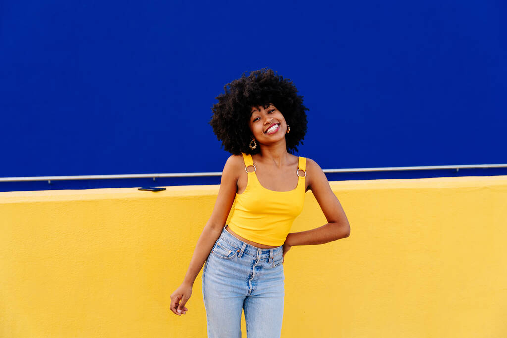 Mulher africana feliz bonita jovem com penteado encaracolado afro passeando na cidade - Retrato estudante preto alegre no fundo da parede colorido - Foto, Imagem