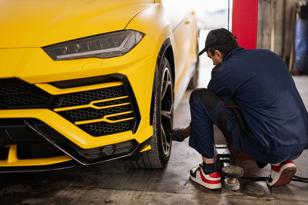 Mecánico comprueba la presión de los neumáticos en amarillo deportivo coche suv. - Foto, imagen