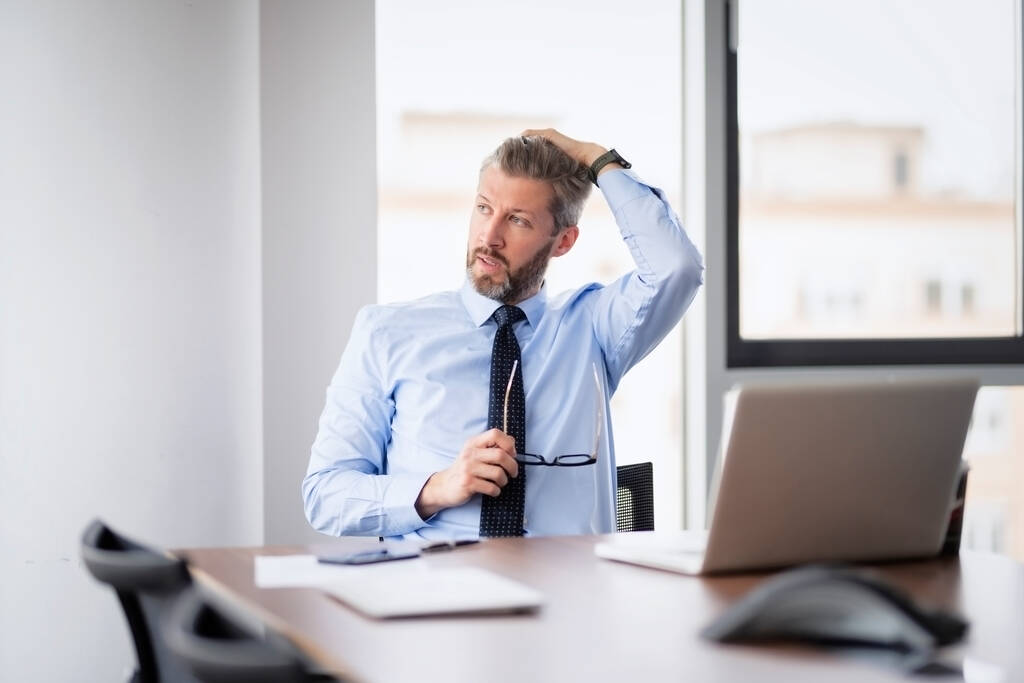 Втомлений середнього віку бізнесмен працює в офісі і використовує ноутбук. Професійний чоловік виглядає тривожним
. - Фото, зображення