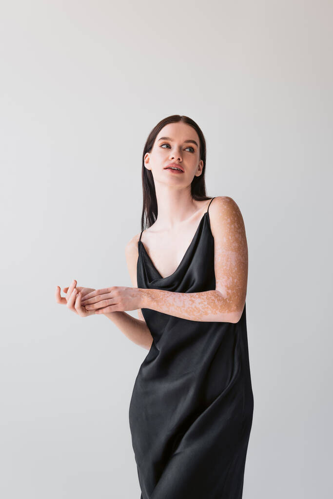 Kobieta zmysłowa z bielactwo pozowanie w czarnej satynowej sukience izolowane na szarości  - Zdjęcie, obraz
