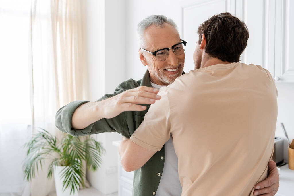 happy mature man in eyeglasses embracing young son at home - Photo, Image