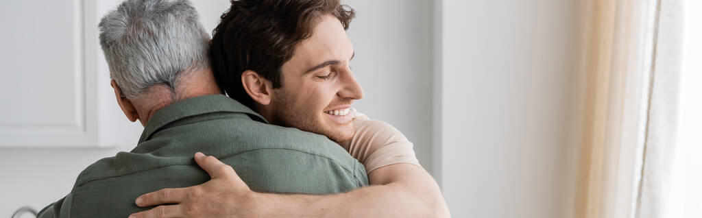 счастливый молодой человек обнимает зрелого и седого отца дома, баннер - Фото, изображение
