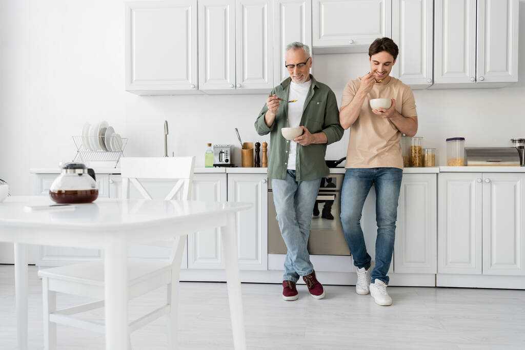 plná délka zralého otce a malého syna snídaní při stání v moderní kuchyni  - Fotografie, Obrázek