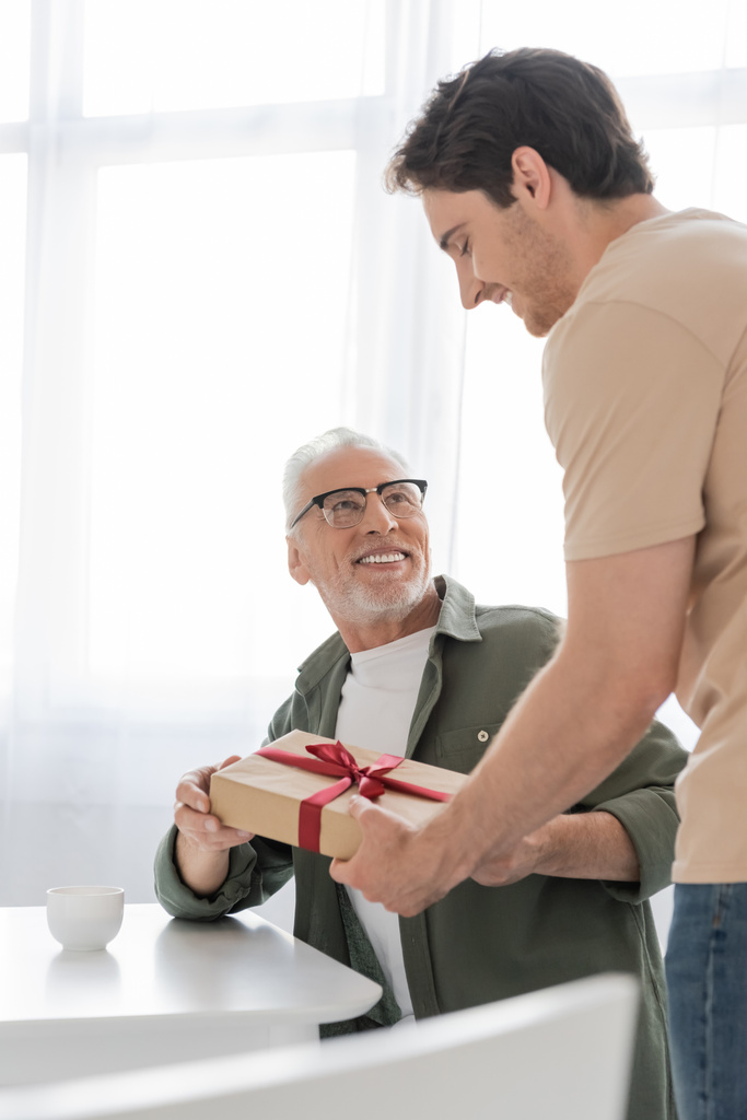 счастливый зрелый мужчина в очках забирает подарок на день отца от маленького сына - Фото, изображение
