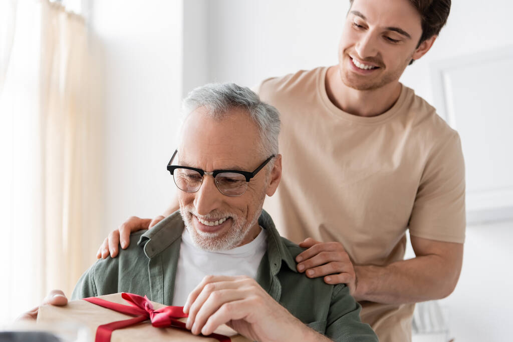 smiling man touching shoulders of happy dad opening fathers day present - Photo, Image