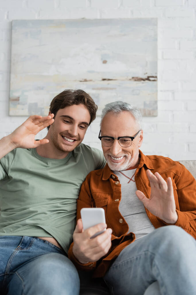 happy mature man and cheerful son waving hands during video call on smartphone  - Photo, Image