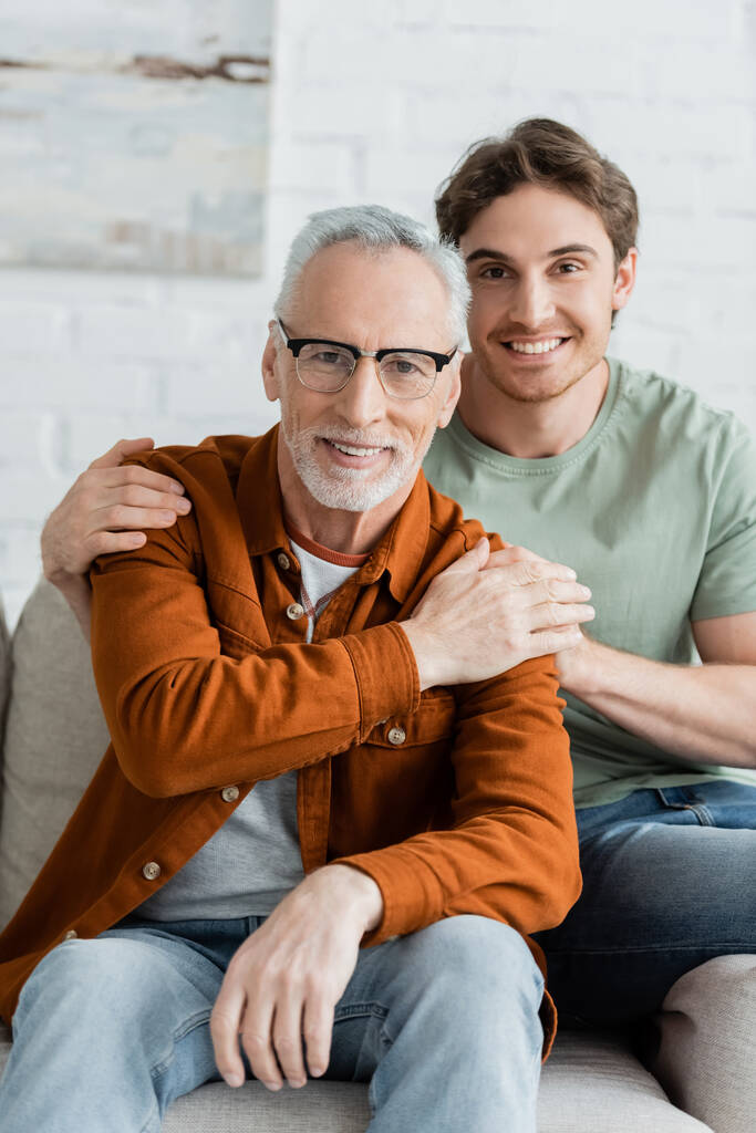 веселий молодий чоловік обіймає бородатого і зрілого батька в окулярах
  - Фото, зображення
