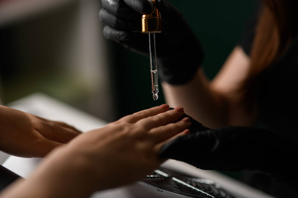 Selektiver Fokus auf Tropfer mit Nagelpflegeöl über weiblicher Hand. Haut- und Nagelpflege. Maniküre. Schönheitssalon - Foto, Bild