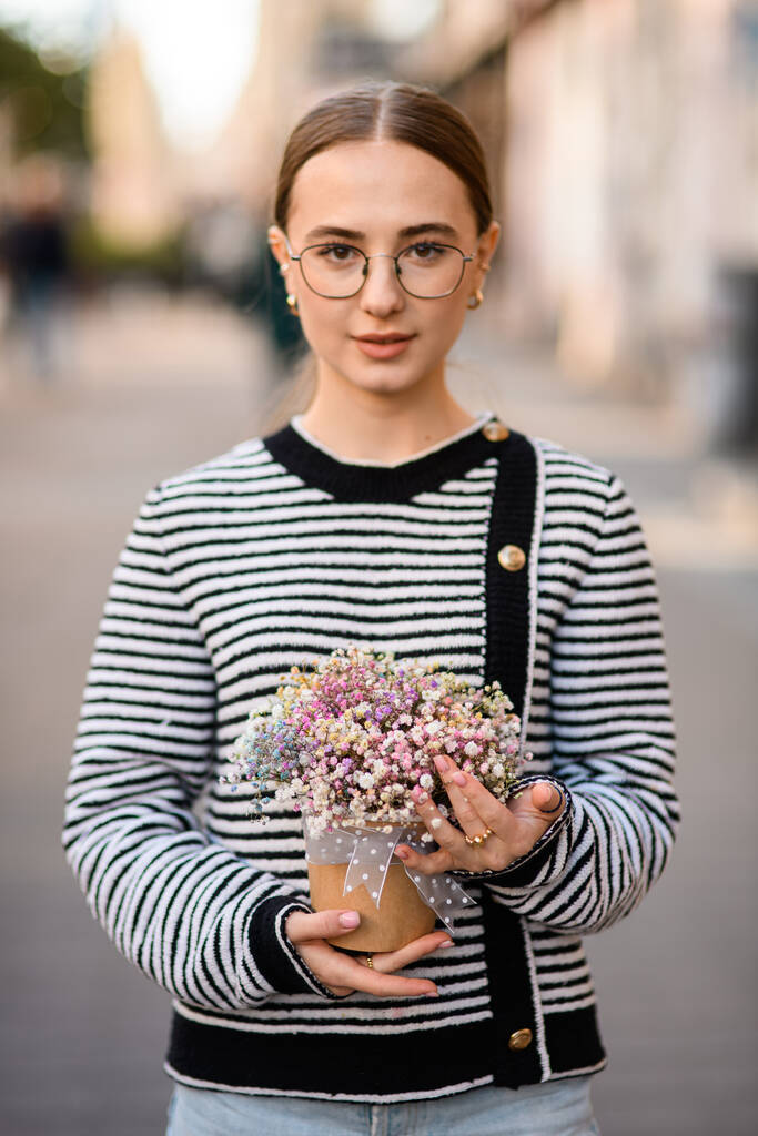 чудовий портрет молодої красивої жінки, що тримає горщик з квітковим розташуванням різнокольорових квітів гіпсофіли в руках
 - Фото, зображення