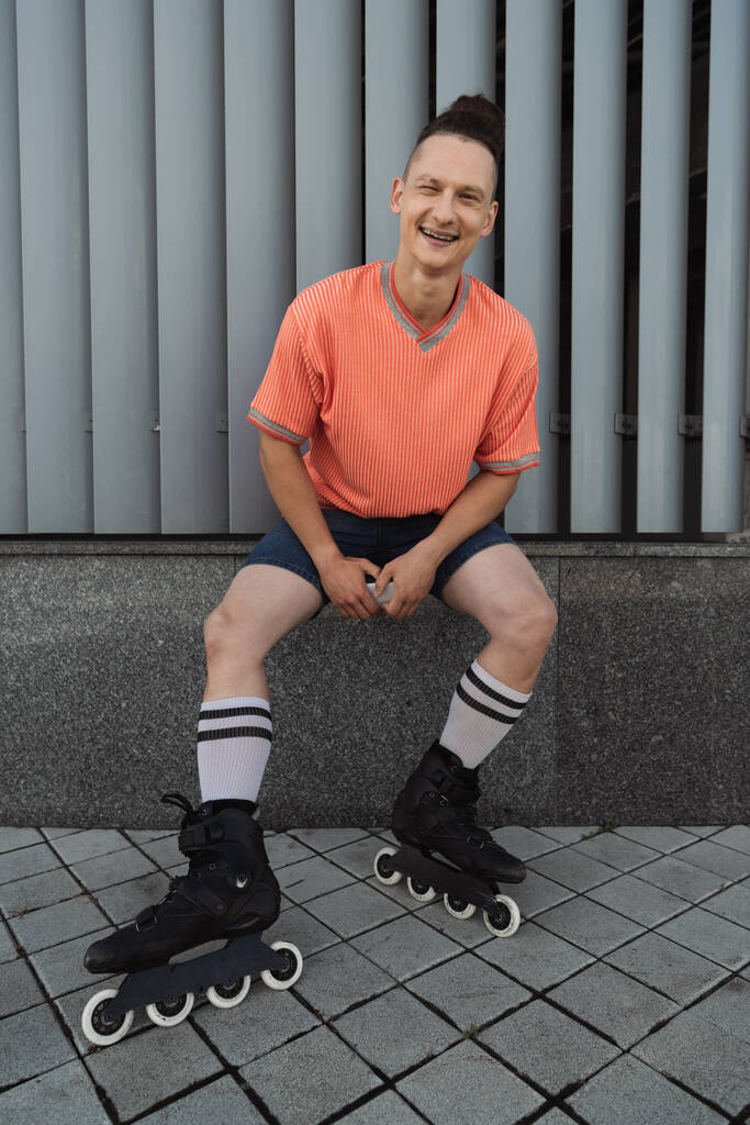 Χαρούμενος άνθρωπος σε casual ρούχα και πατίνια κοιτάζοντας κάμερα σε αστικό δρόμο  - Φωτογραφία, εικόνα