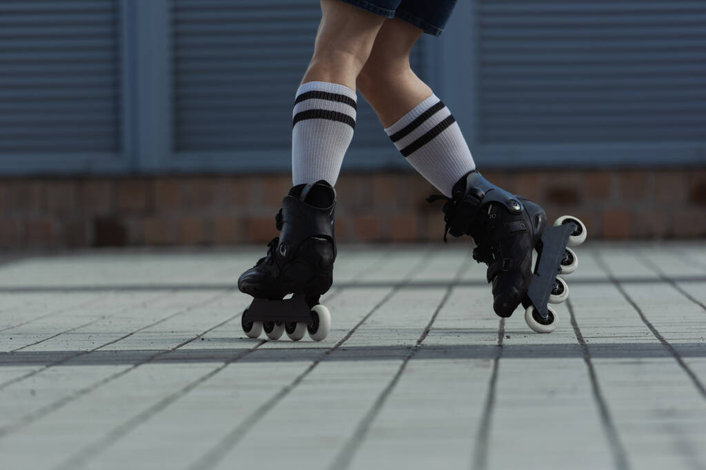 Vista recortada del patinador en calcetines de rodilla y patines montados en la calle  - Foto, imagen