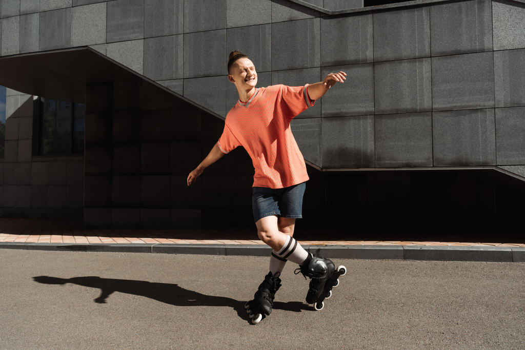 Веселый молодой человек в роликах, стоящий на асфальте на улице  - Фото, изображение