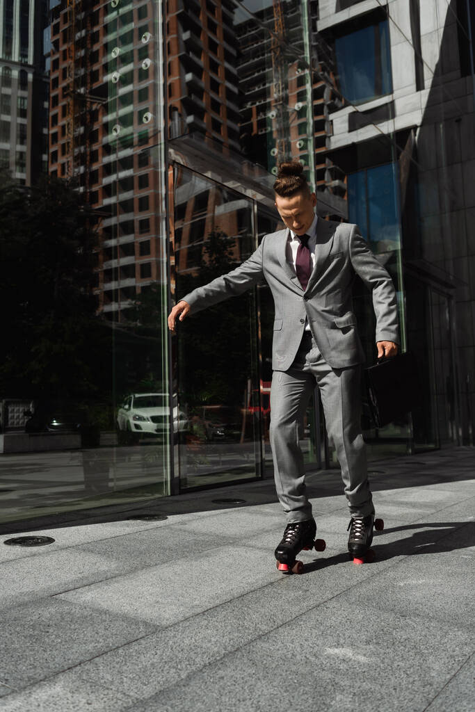 full length of young businessman with trendy hairstyle roller skating on city street - Photo, Image