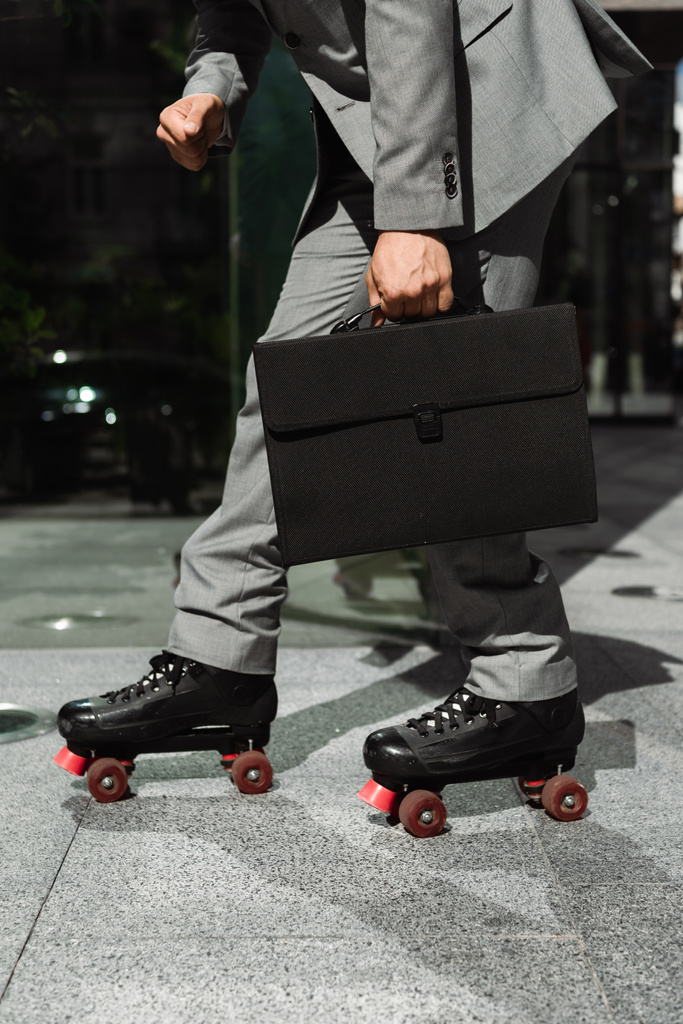 partial view of businessman with black briefcase rollerskating on city street - Photo, Image