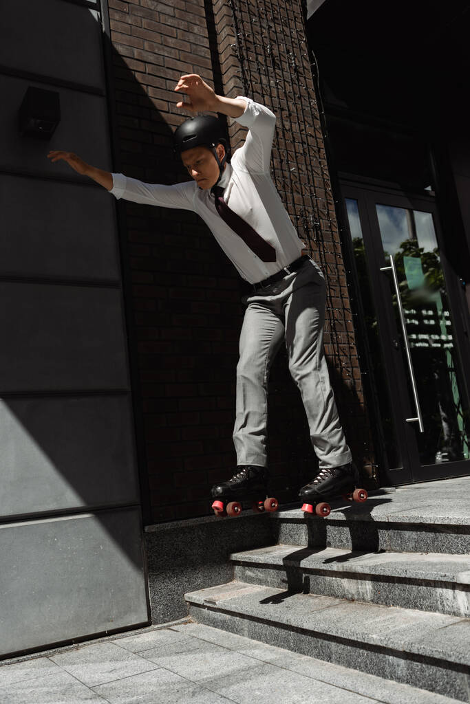 full length of roller skater in formal wear and helmet jumping from stairs on urban street - Photo, Image