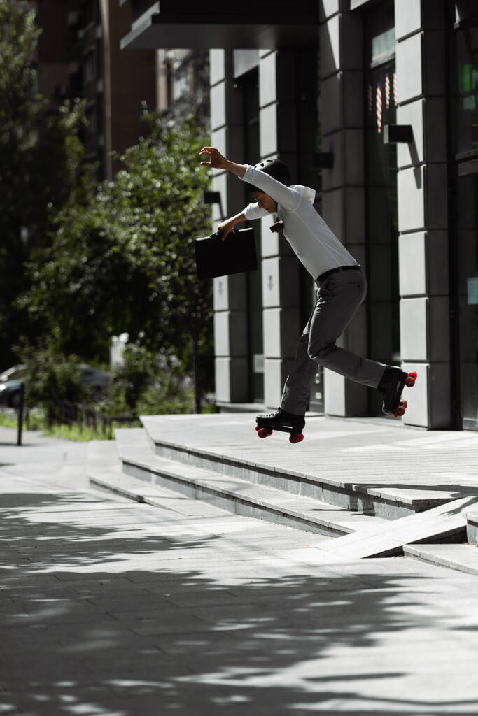 вид збоку молодого бізнесмена в роликових ковзанах і шоломі, що стрибає зі сходів на міській вулиці
 - Фото, зображення