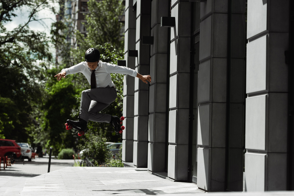 повна довжина бізнесмена в шоломі і роликових ковзанах стрибає, роблячи трюк на міській вулиці
 - Фото, зображення