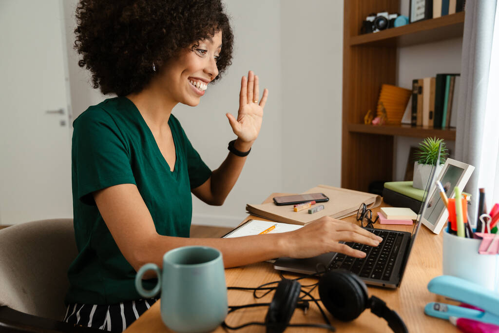 afro-américaine jeune femme avec frisée afro coiffure assis au bureau et en utilisant un ordinateur portable à la maison - Photo, image