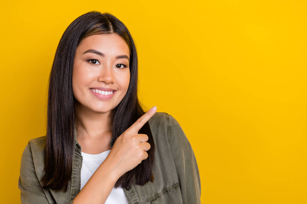 Close-up portret van jonge vrolijke glimlach leuke Indonesische vrouw vinger directe mockup nieuwe winkelcentrum opening geïsoleerd op gele kleur achtergrond. - Foto, afbeelding
