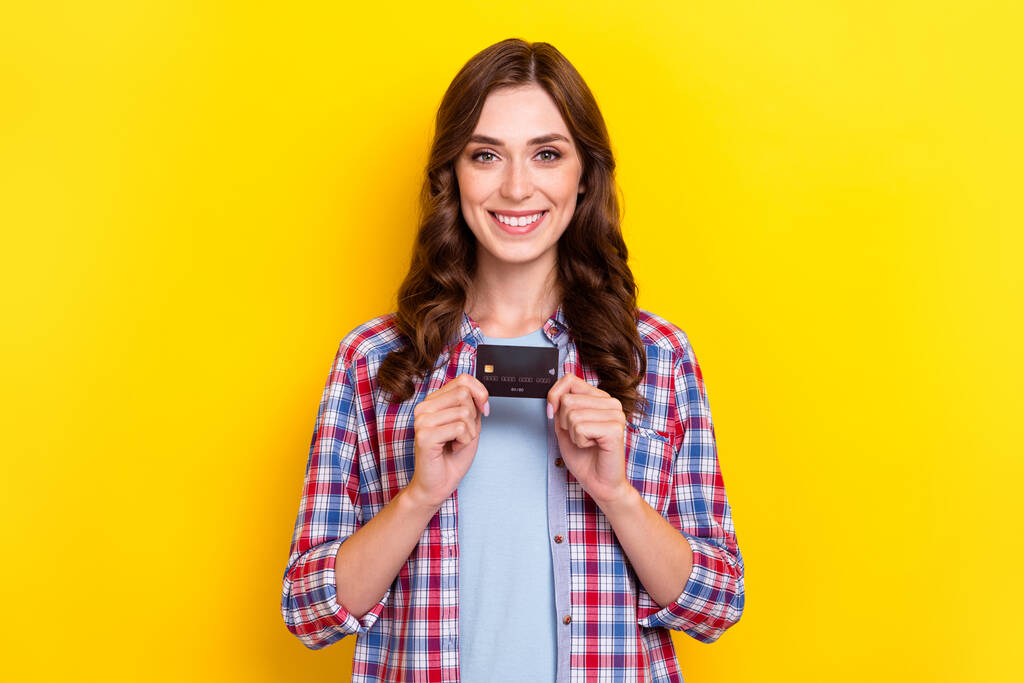 Φωτογραφία του χαριτωμένο γοητευτικό κορίτσι ντυμένος καρό πουκάμισο κρατώντας δείχνει χρεωστική κάρτα απομονωμένο κίτρινο χρώμα φόντο. - Φωτογραφία, εικόνα