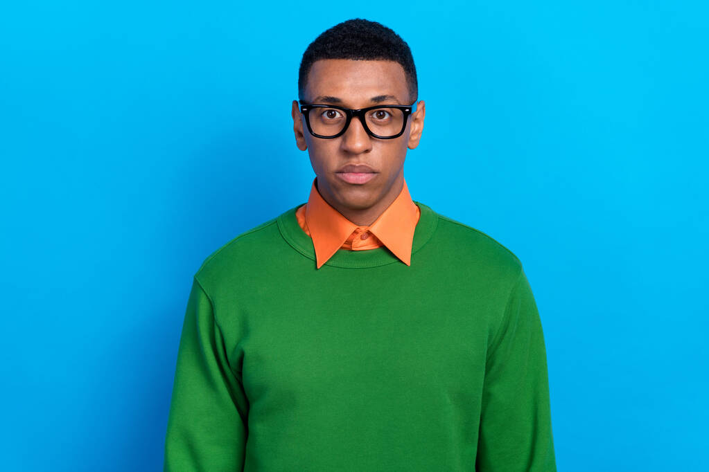 Portret poważnego, pewnego siebie faceta ubranego w pomarańczową koszulę pod zielonym, pulowerowym okularem popatrz na kamerę odizolowaną na niebieskim tle. - Zdjęcie, obraz