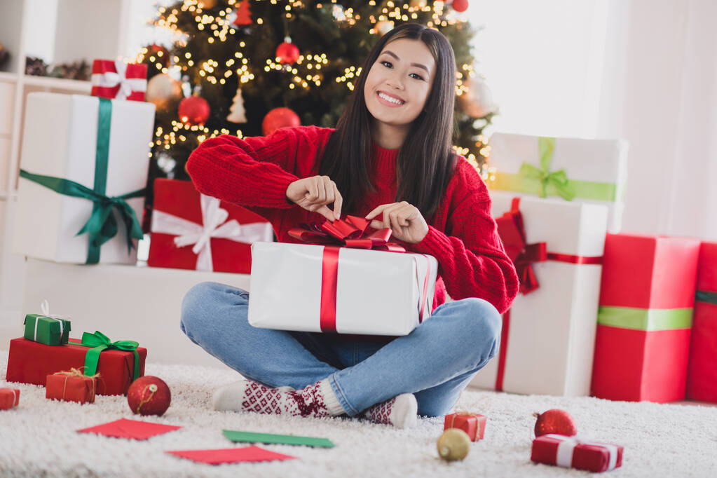 Foto von süßen entzückenden Mädchen tragen xmas roten Pullover Öffnung noel Geschenkbox lächelnd drinnen Home Room. - Foto, Bild