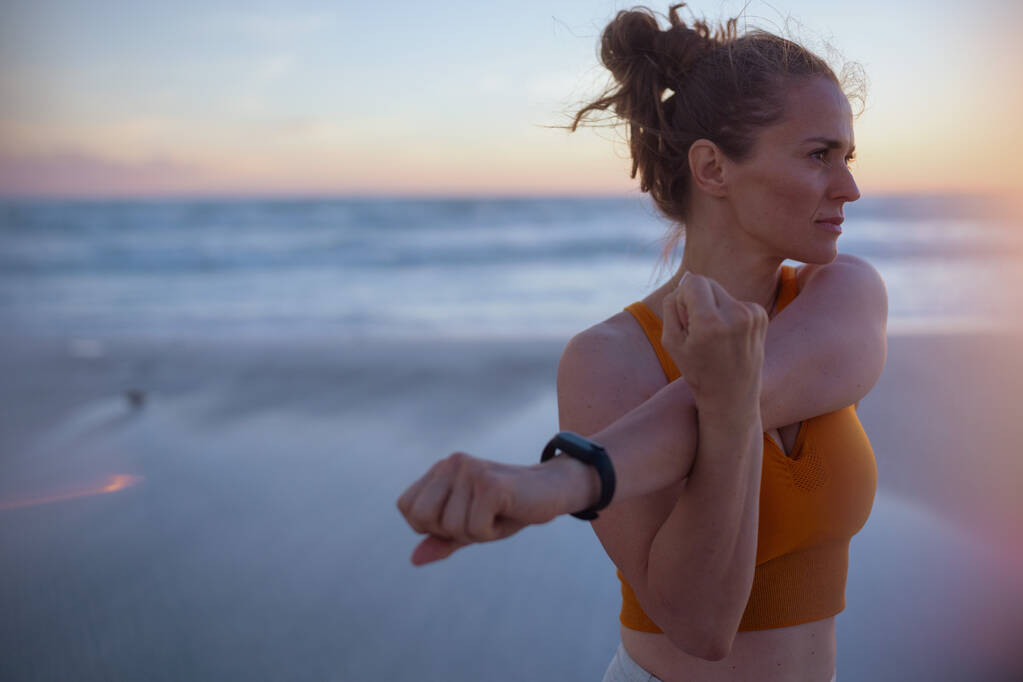 fit vrouw jogger in sport kleding met fitness tracker op het strand bij zonsondergang. - Foto, afbeelding