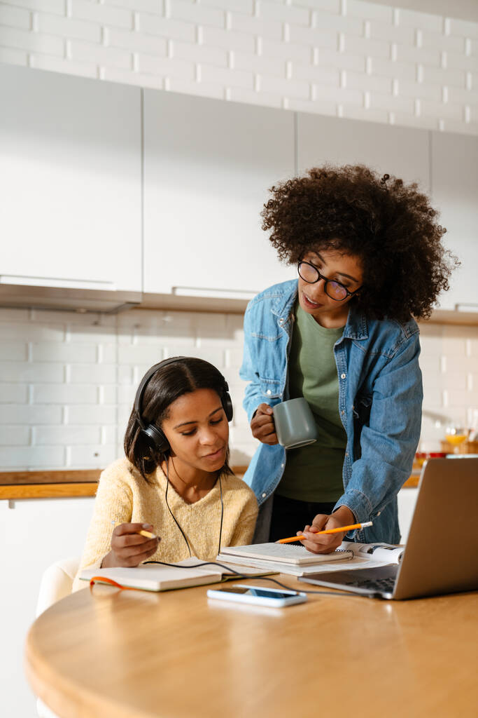 若いアフリカ系アメリカ人の女性と彼女の十代の娘は一緒に家で宿題をする - 写真・画像