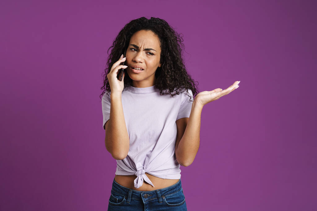 Молодая черная женщина разговаривает по мобильному телефону и держит копирайс изолированы на фиолетовом фоне - Фото, изображение