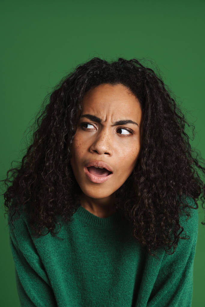 Молода чорна жінка з хвилястим волоссям виражає сюрприз на камеру ізольовано на зеленому фоні
 - Фото, зображення