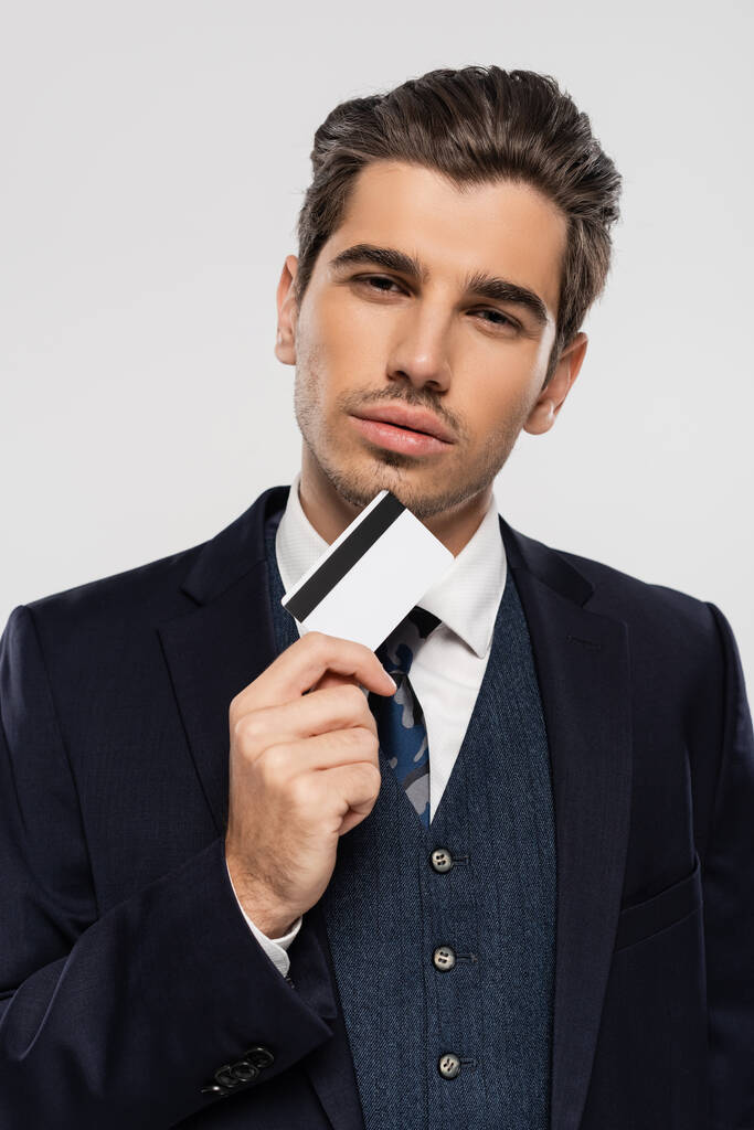 homme d'affaires réussi en costume tenant la carte de crédit et regardant la caméra isolée sur gris - Photo, image