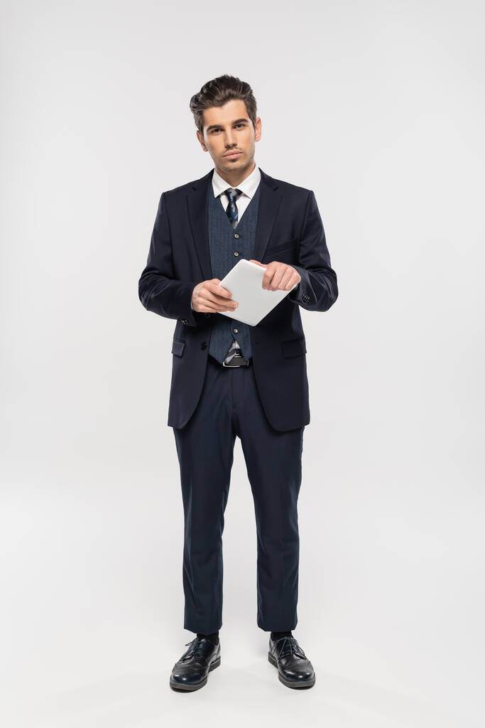 longitud completa del exitoso hombre de negocios en traje que sostiene la tableta digital en gris  - Foto, imagen