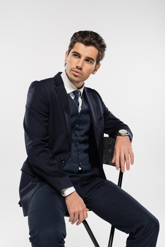 joven hombre de negocios en ropa formal sentado en la silla mientras posando aislado en gris - Foto, Imagen