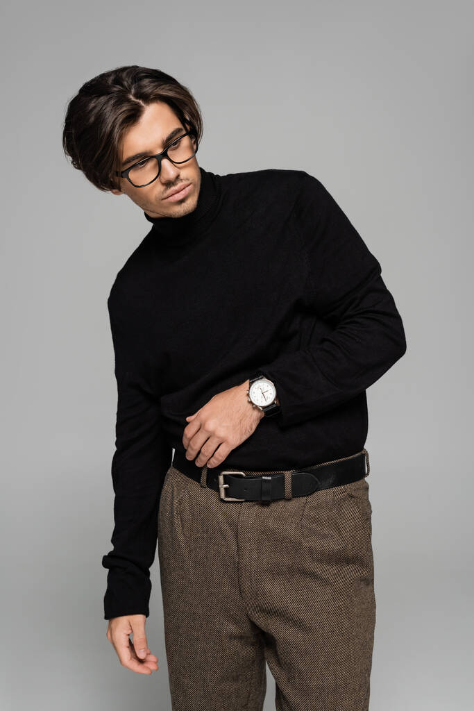 brunette man in black turtleneck and pants posing in eyeglasses isolated on grey - Photo, Image