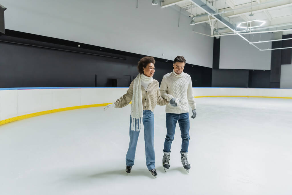 Junges gemischtrassiges Paar hält Händchen beim Schlittschuhlaufen auf Eisbahn  - Foto, Bild