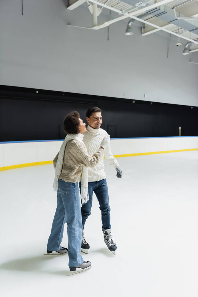 Joven mujer afroamericana patinaje sobre hielo mientras pasa tiempo con su novio en la pista de patinaje  - Foto, imagen