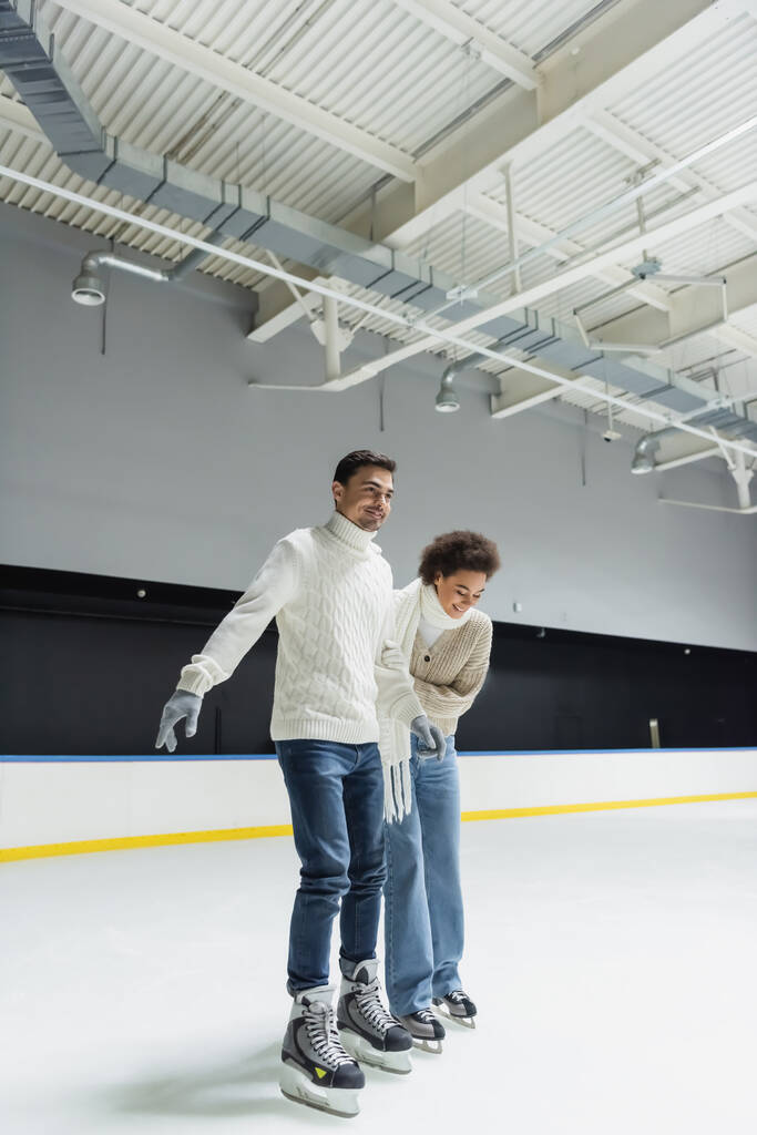 Femme afro-américaine souriante patinage sur glace avec petit ami sur la patinoire  - Photo, image