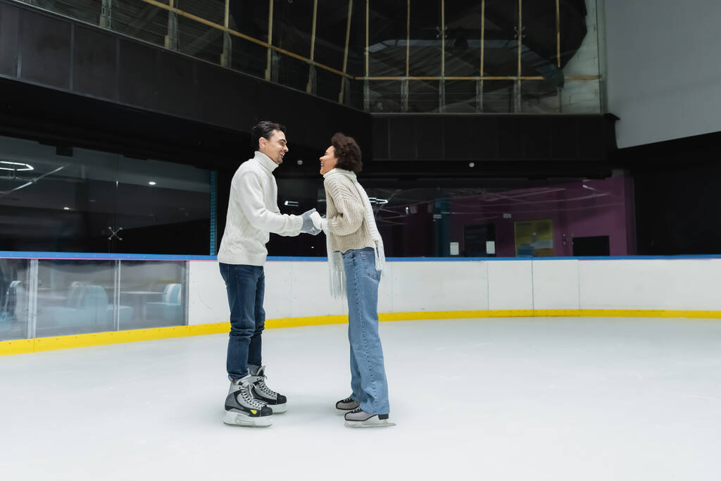 Vue latérale du couple interracial joyeux passer du temps pendant la date sur la patinoire  - Photo, image